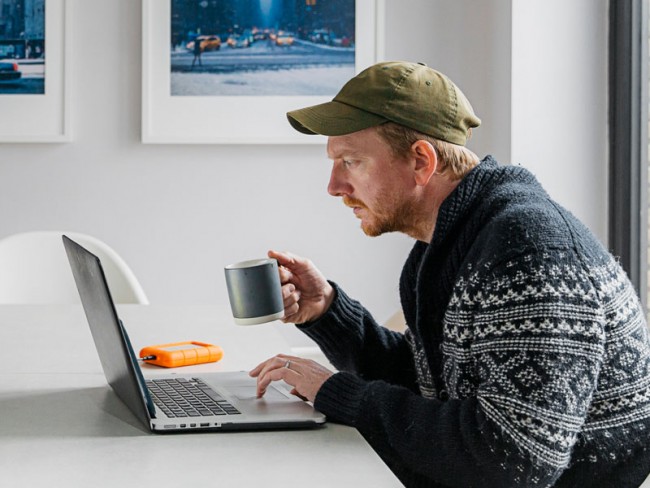 Man at kitchen table drinking coffee and taking an online course from home