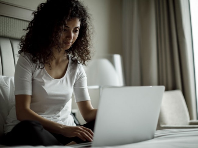 Young adult woman using a computer on her bed